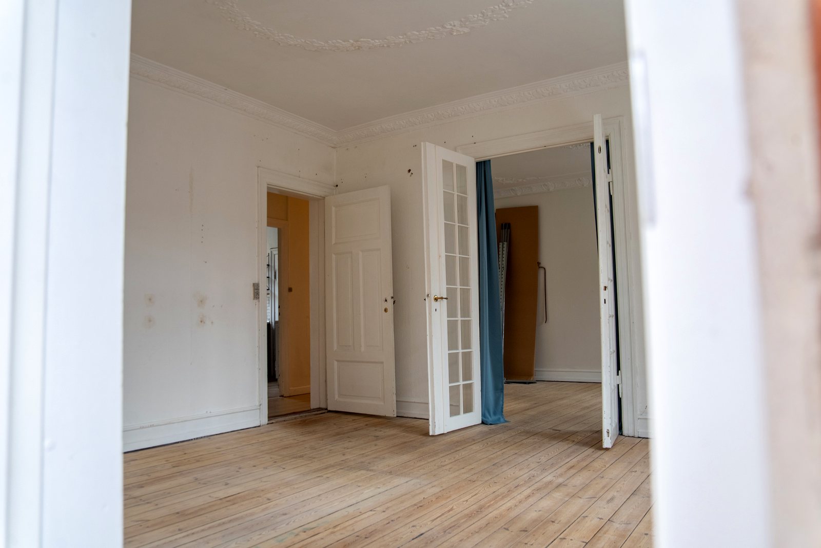 Stuen med trætte vægge, franske døre og gammelt gardin